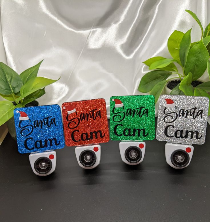 four small cameras sitting next to each other on top of a black table with green plants in the background