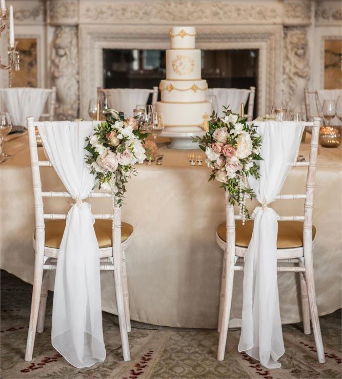 the table is set with two white chairs and flowers on each chair, along with a wedding cake