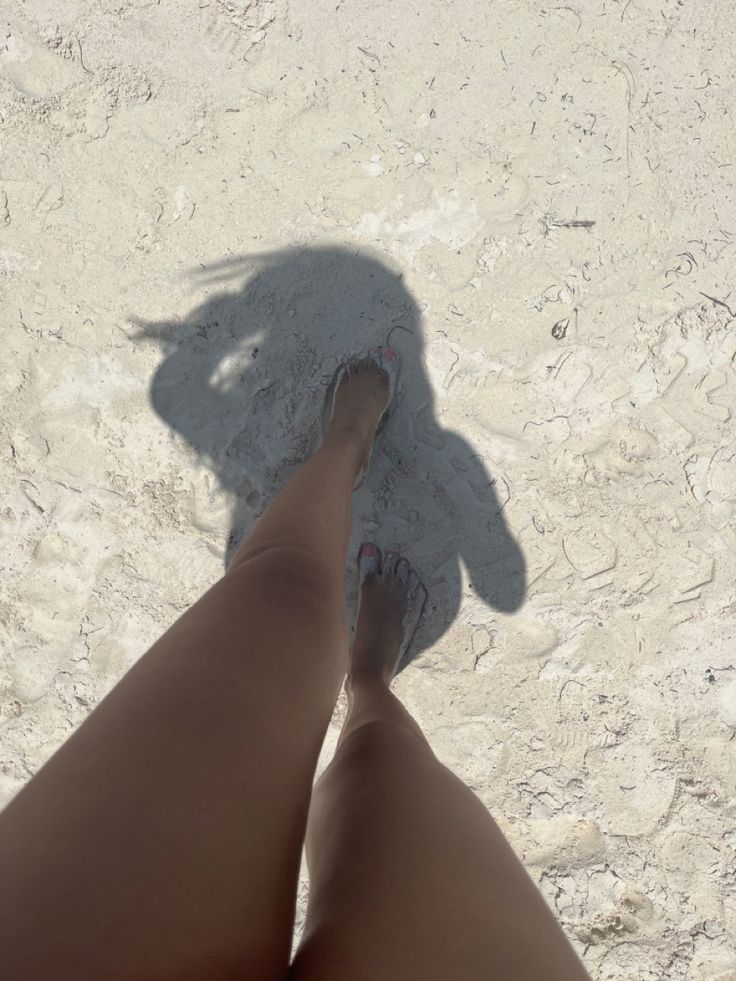 the shadow of a person's legs and feet on white sand