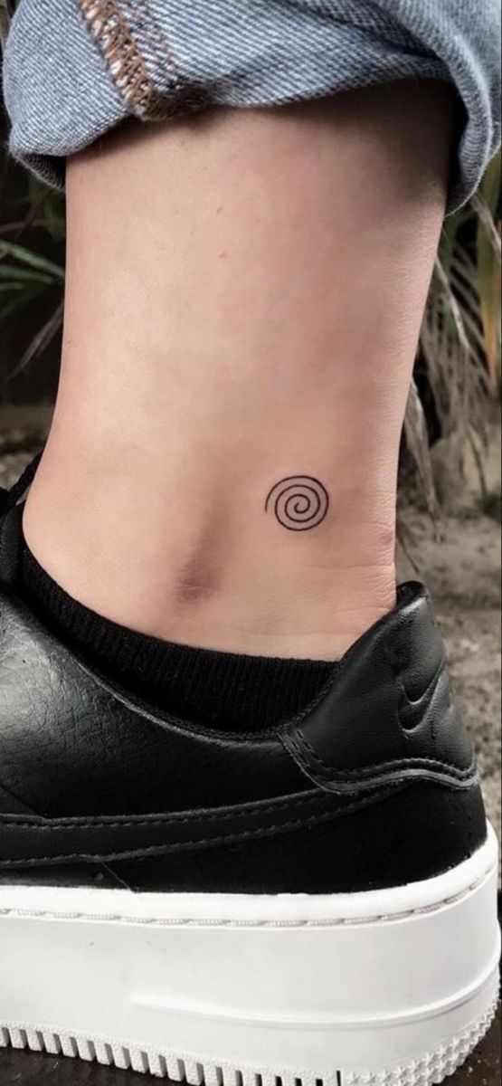 a woman's ankle with a small spiral tattoo on her left side ribcage