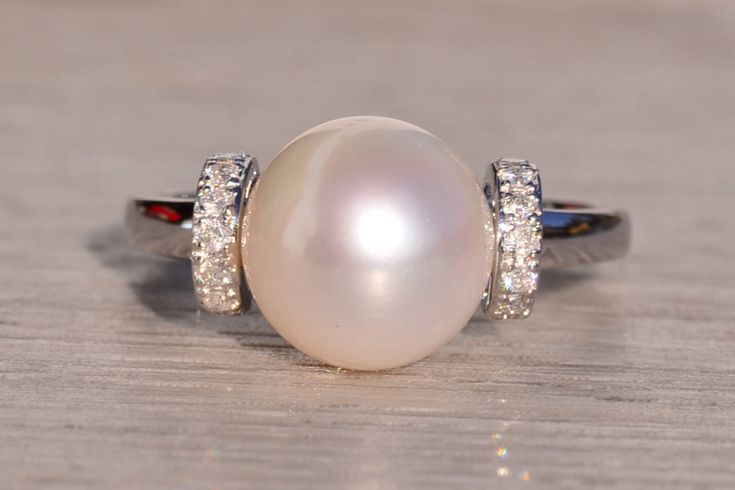 The Denali Mountain: Akoya Pearl and Natural Diamond Ring in White Gold. This exquisite ring showcases a lustrous 9.5mm cultured Akoya pearl nestled between two elevated shoulders adorned with 0.06 carats of round-cut natural diamonds, adding a touch of sparkle and sophistication to the design. Crafted with precision in 14 karat white gold, the ring exudes timeless elegance and charm. Currently sized at 7, it offers the option for personalized adjustment to any finger size, with an additional ch Elegant Akoya Pearl Oval Rings, Elegant Oval Akoya Pearl Rings, Elegant Oval Pearl Ring With Diamond Accents, Elegant Oval Pearl Ring With Brilliant Cut, Elegant Oval Brilliant Cut Pearl Ring, Elegant Akoya Pearl Rings In Diamond White, Elegant Pearl White Rings With Brilliant Cut, Elegant Pearl Ring With Diamond Accents For Formal Occasions, Elegant White Round Cut Pearl Ring