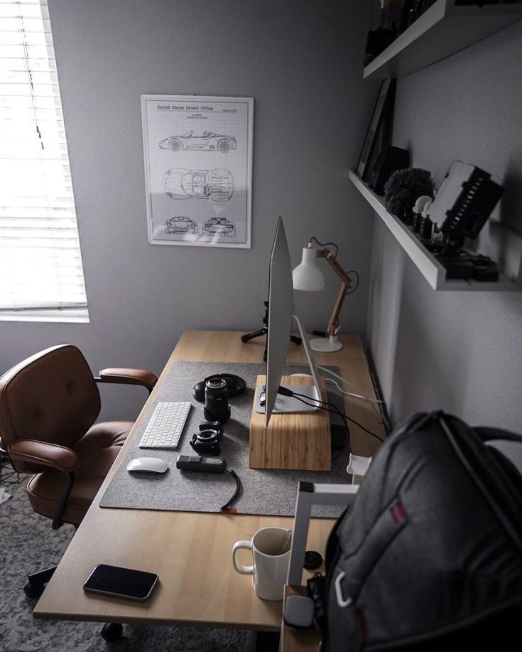 a desk with a laptop, monitor and coffee cup on it in front of a window