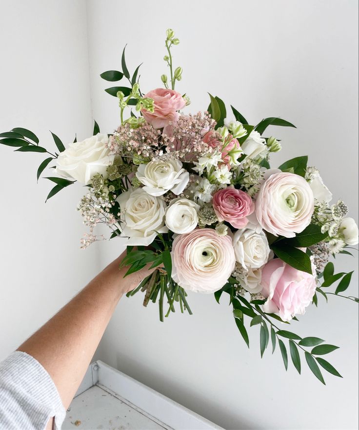 a bouquet of flowers being held up by someone's hand in front of a white wall