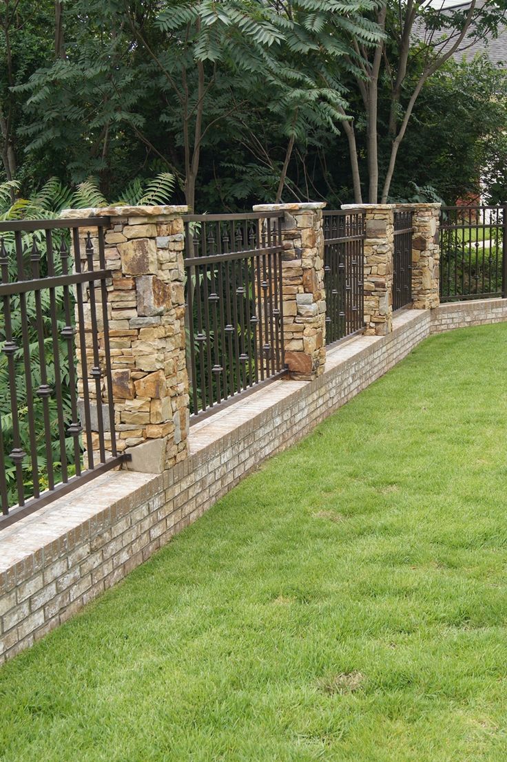 a stone wall and metal fence in the grass