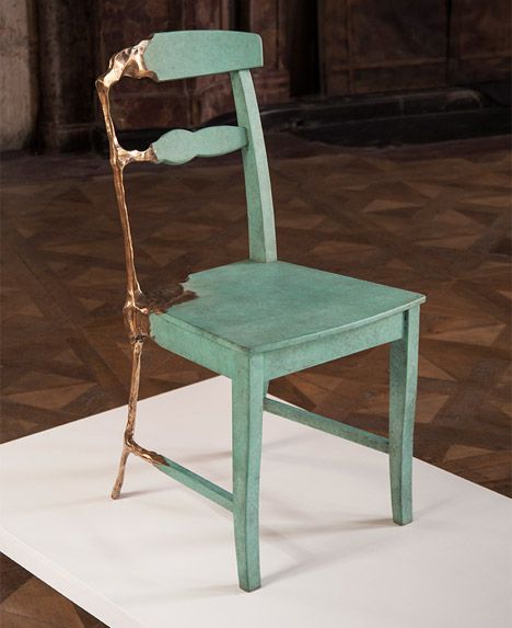 a green chair sitting on top of a white floor next to a wooden structure with a gold stick sticking out of it's back end