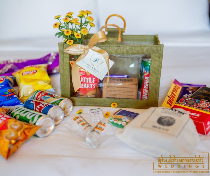 an assortment of candy and snacks on a bed with flowers in the bag next to it