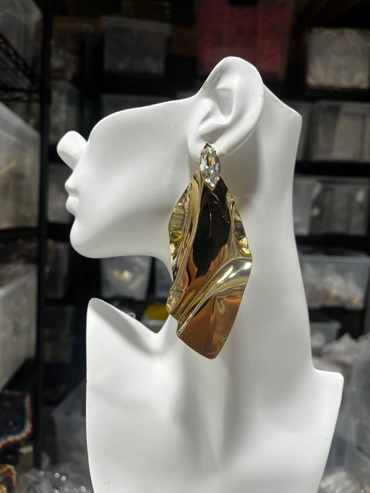 Unveiling the "Golden Drift Abstract Earring," a masterpiece of fluid artistry and contemporary design. This single statement earring features a bold, sculptural form that resembles a cascade of molten gold, frozen in time. The lustrous, high-shine finish captures and reflects light, creating a mesmerizing effect that is sure to turn heads. At the pinnacle, a subtle yet striking crystal adds a touch of refined sparkle, anchoring the piece with an air of sophistication. Designed for the bold and the fashion-forward, this earring is a conversation starter, perfect for elevating any ensemble with its avant-garde charm. Sculptural Gold Jewelry For Gifts, Elegant Metallic Earrings For Gift, Gold Dangle Wrap Earrings For Party, Elegant Irregular Jewelry For Party, Sculptural Gold Jewelry For Gift, Gold Metal Wrap Earrings For Party, Gold Drop Wrap Earrings For Party, Gold Drop Earrings For Party, Modern Twist Gold Jewelry For Party