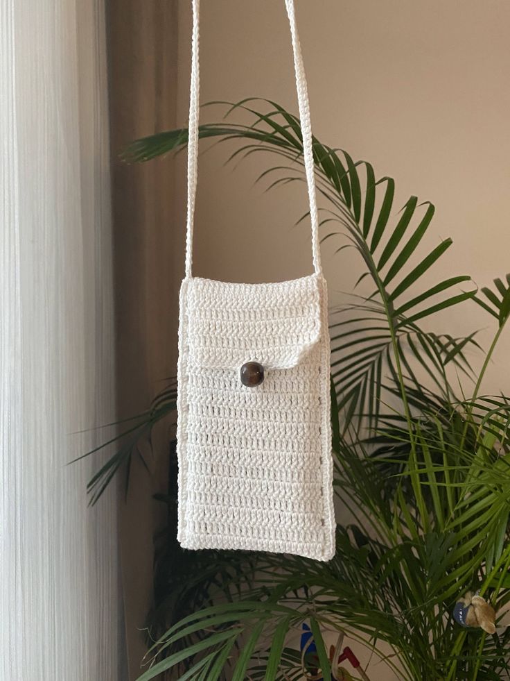 a white crocheted bag hanging from a hook on a wall next to a potted plant