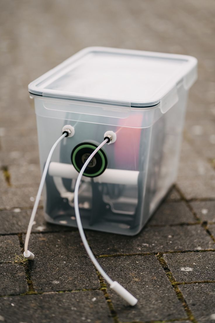 a plastic container sitting on the ground next to a pair of ear buds and wires