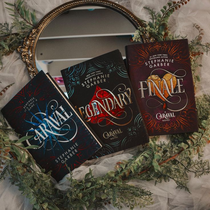 three books sitting on top of a white sheet next to a round metal frame with greenery around it