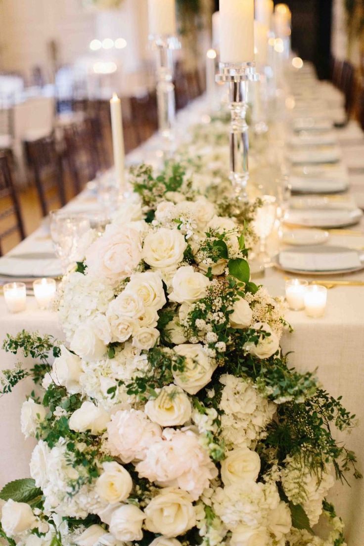 a long table with white flowers and candles on the top is set for a formal dinner