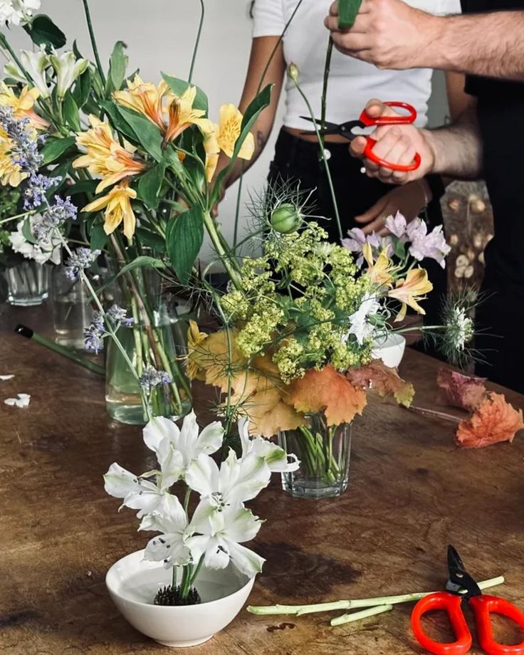 two people are cutting flowers in vases on a table with scissors and shears