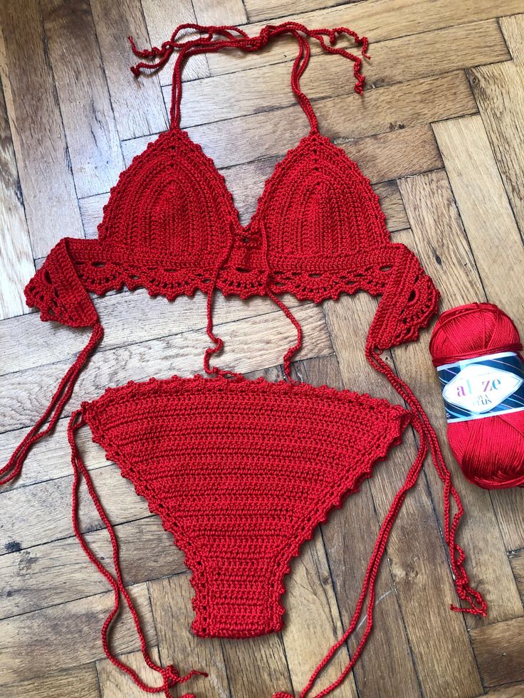 two pieces of red crochet swimsuit on wooden floor next to ball of yarn