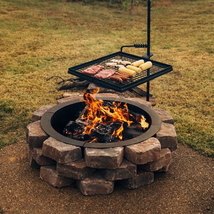 an outdoor grill with meat and vegetables cooking over it's fire pit in the middle of a grassy area