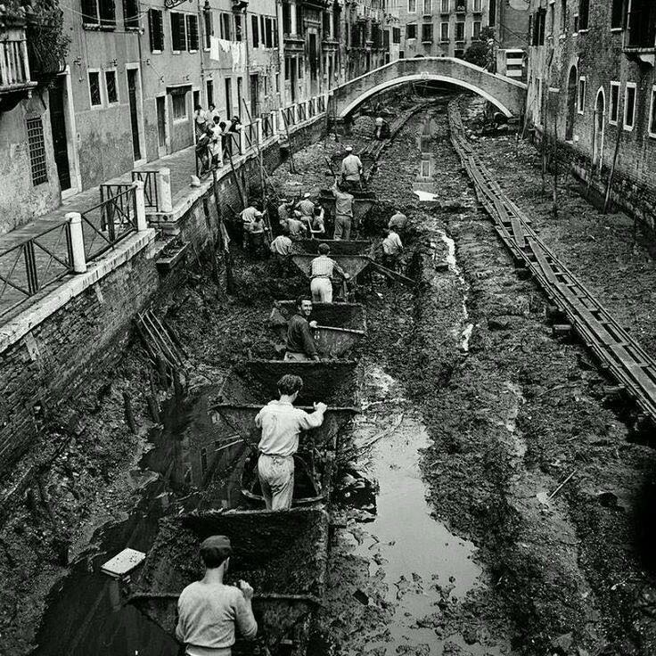 an old black and white photo of people working in the water next to some buildings