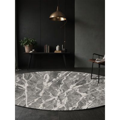 a round rug with grey and white marble on the floor in front of a black wall