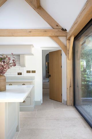 an open kitchen and dining room area with white counter tops, wood beams and wooden ceilinging