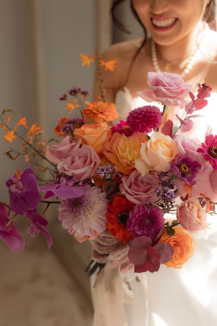 a bride holding a bouquet of flowers in her hand and smiling at the camera with sunlight streaming through