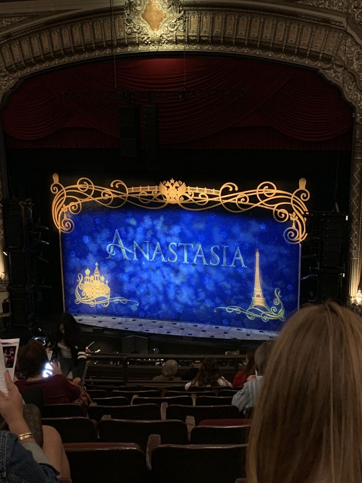 people are taking pictures on their cell phones in front of an ornate theater screen with the words anastasia written on it