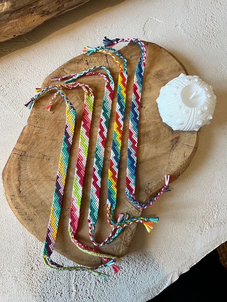 multicolored striped necklaces are on a wooden plate next to a white cup