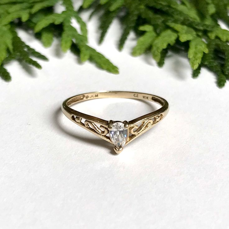 a gold ring with a heart shaped diamond in the center on a white surface surrounded by green leaves