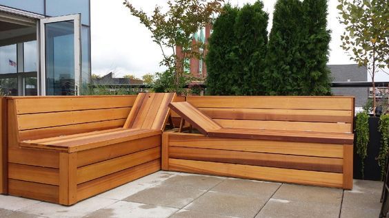 a wooden bench sitting on top of a cement floor next to trees and bushes in front of a building