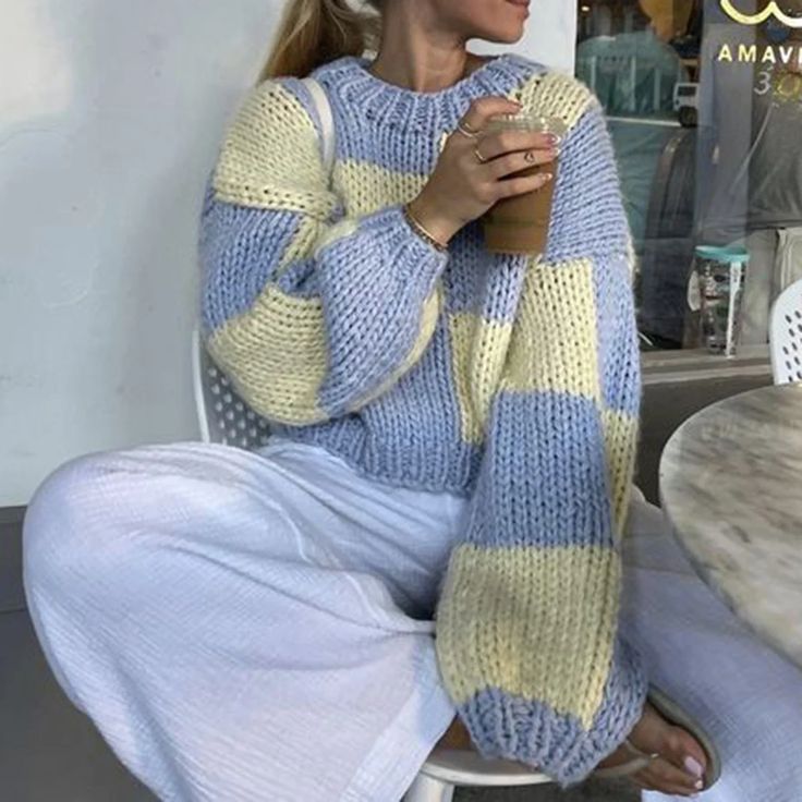 a woman sitting on a chair holding a cup and wearing a blue and yellow striped sweater