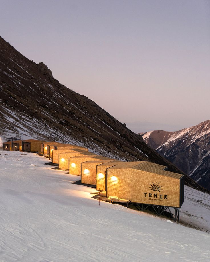 a group of tents sitting on top of a snow covered slope next to a mountain