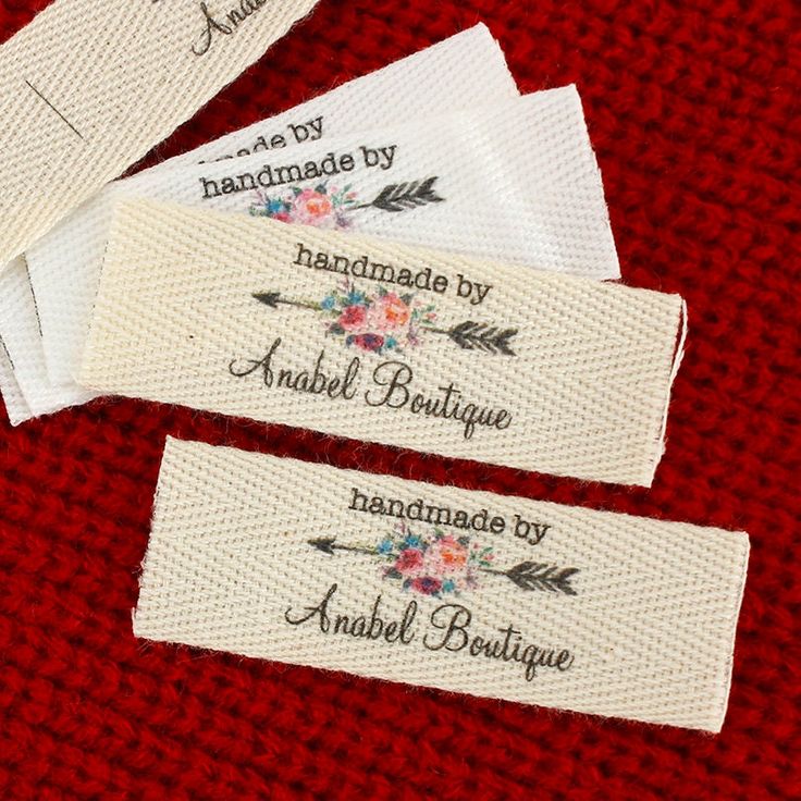 three labels with flowers and arrows are on a red surface, one has the words handmade by anubel boutique written in black ink