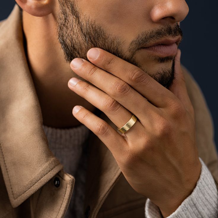 a man with a ring on his finger looking off to the side while wearing a trench coat