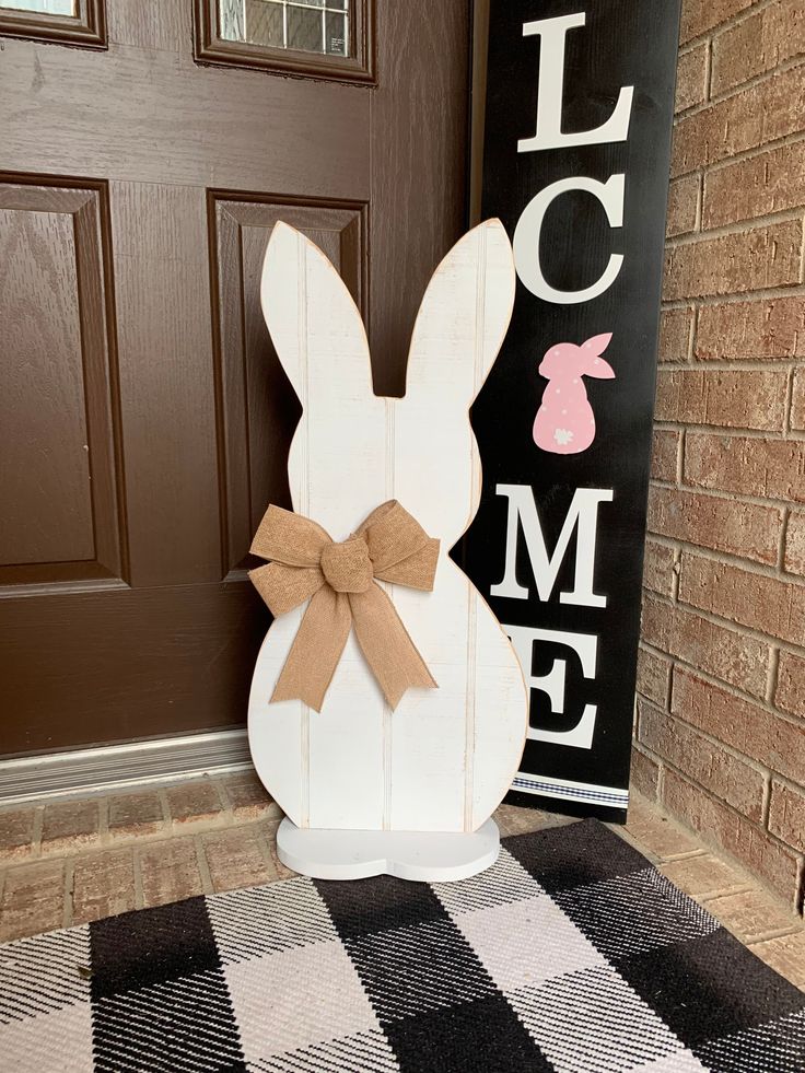 a white wooden bunny sitting on top of a black and white checkered door mat