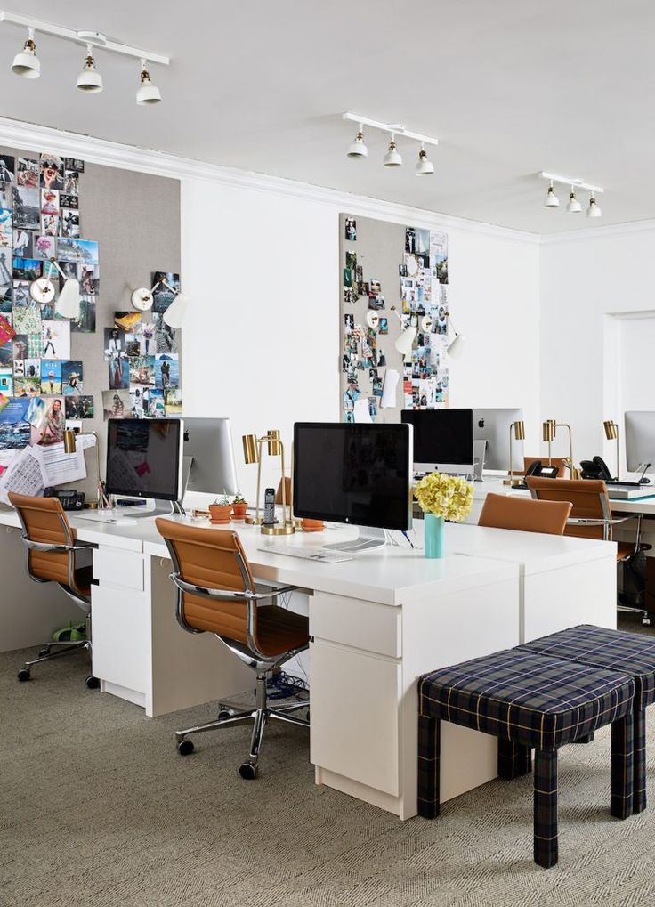 an office with multiple desks and computer screens on the wall, along with two stools