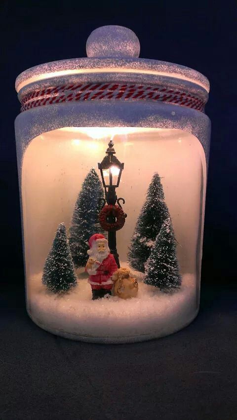 a glass jar filled with snow covered trees and a santa clause figurine in it