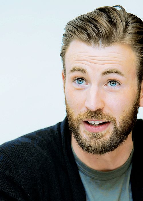 a man with a beard and blue eyes looks at the camera while wearing a black sweater