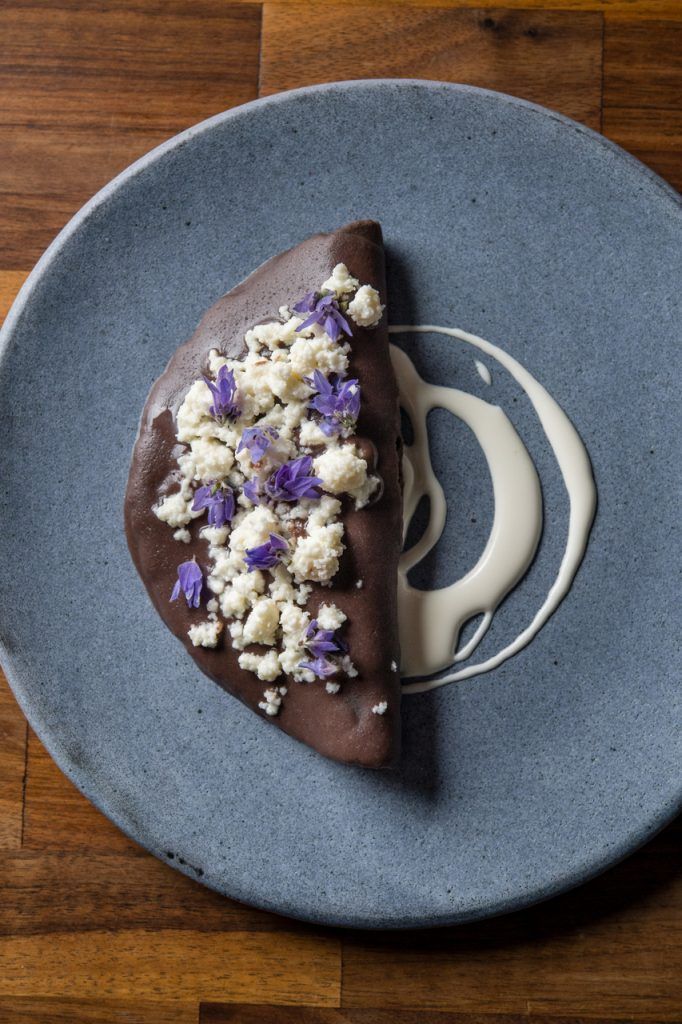 a piece of chocolate cake on a blue plate with white and purple flowers in the middle