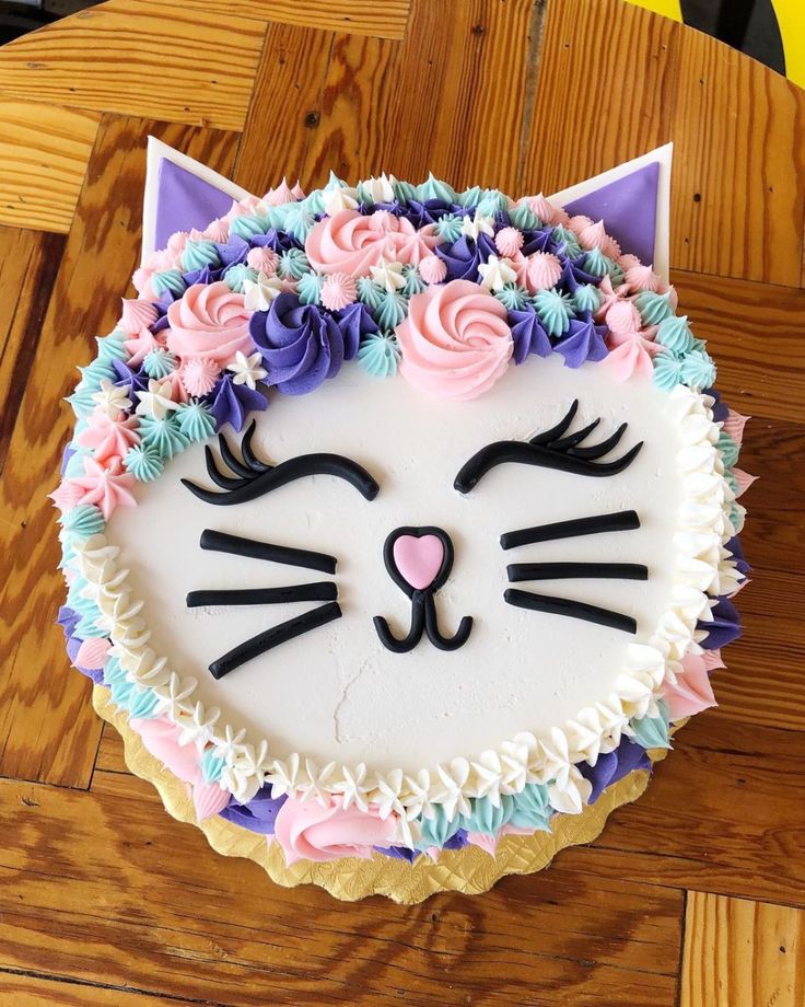 a cake decorated to look like a cat with flowers around its face and eyes, sitting on a wooden table