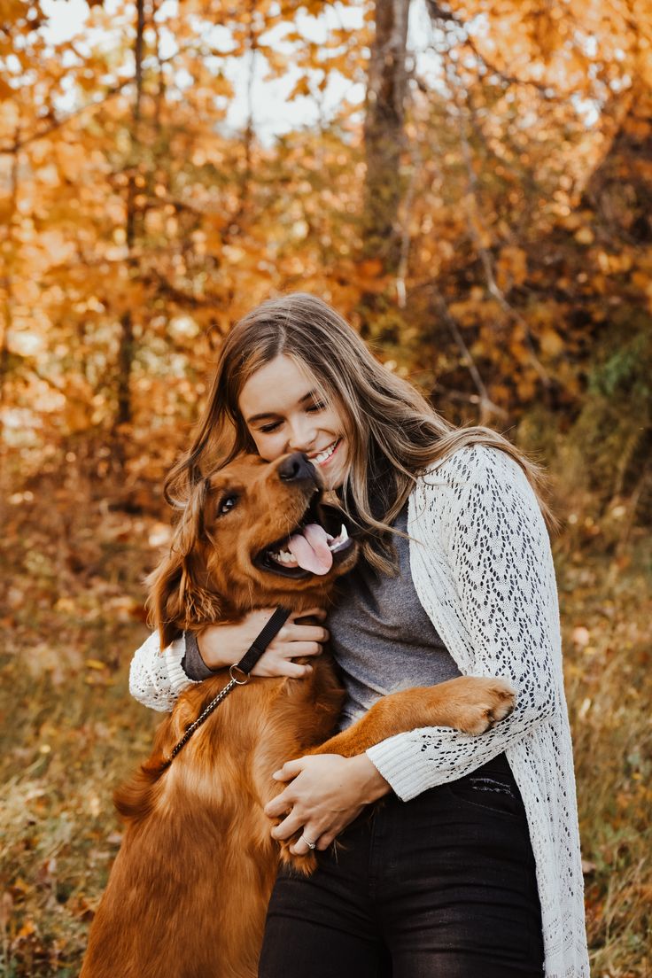 a woman is hugging her dog in the fall leaves while she holds it up to her face