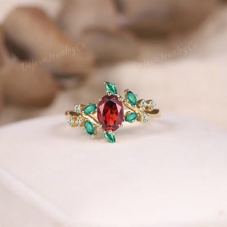 a close up of a ring with a red stone and green leaves on the side