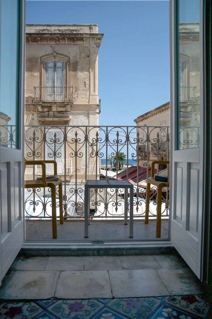 an open door leading to a balcony with two chairs and a table in front of it