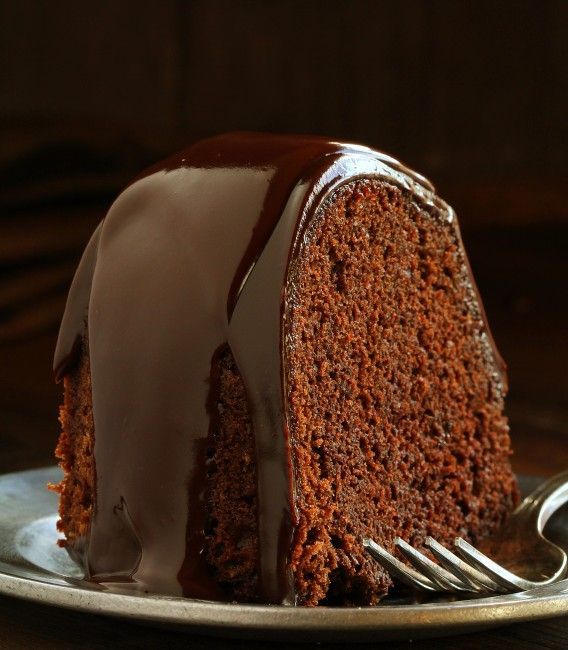 a slice of chocolate cake on a plate with a fork next to it and drizzled with icing