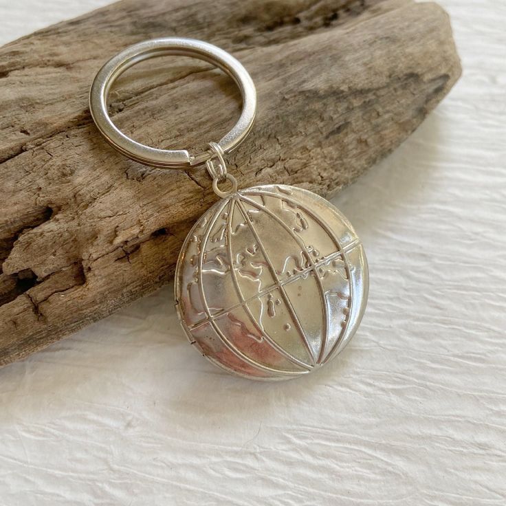 a silver keychain with a compass on it sitting next to a piece of driftwood