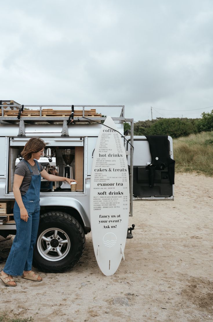 a woman standing next to a surfboard in front of a truck on the beach