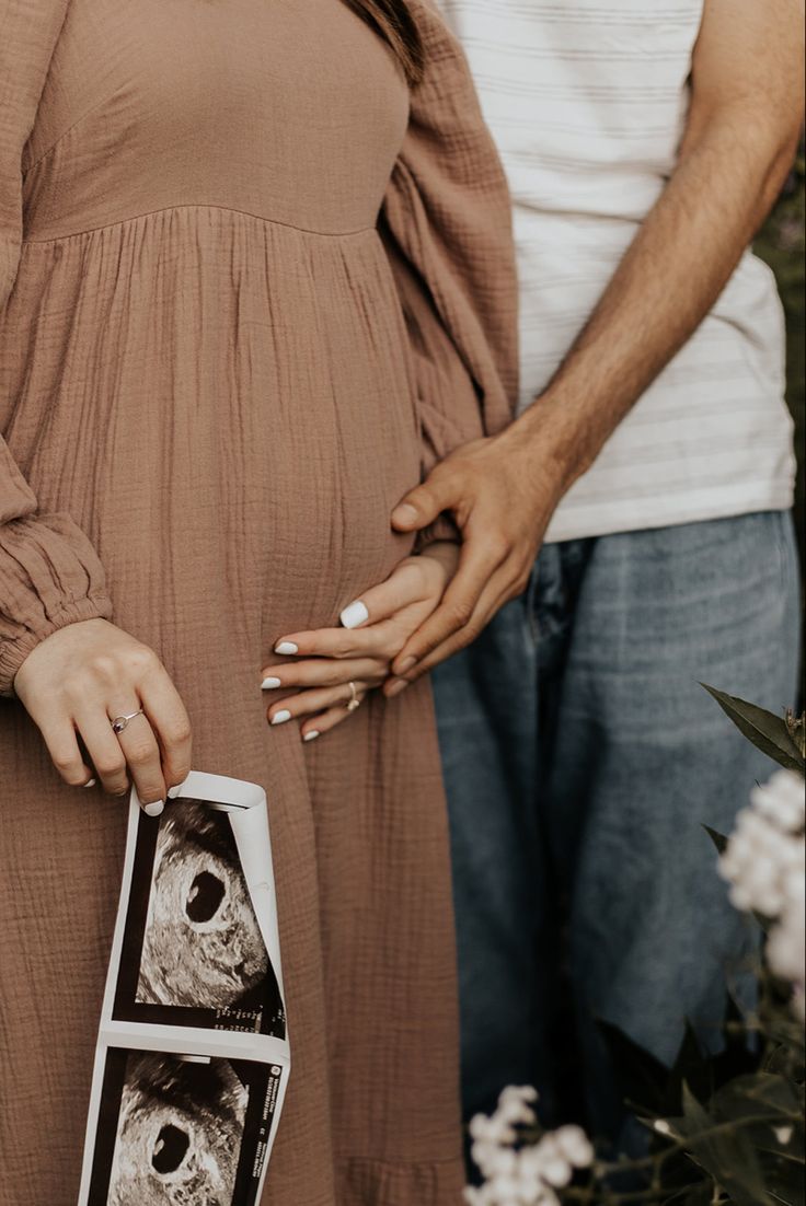 Man holding woman’s hand over her belly over her pink dress, in the womans other hand holds and ultrasound, the picture cuts off right before their heads Things To Do With Ultrasound Pictures, Maternity Pictures With Ultrasound, Maternity Shoot With Sonography, Ultrasound Photo Announcement, Maternity Shoot Ultrasound, Pregnancy Announcement Pictures Without Ultrasound, Maternity Pictures Ultrasound, Studio Baby Announcement, First Ultrasound Picture Ideas