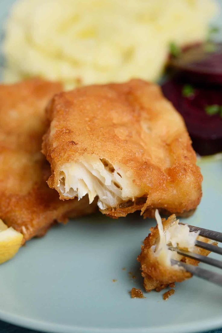 a piece of fried fish is being eaten with a fork and some mashed potatoes are in the background