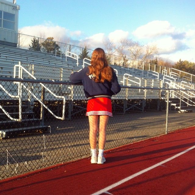 a woman standing on a tennis court with her arms behind her back and looking at the bleachers