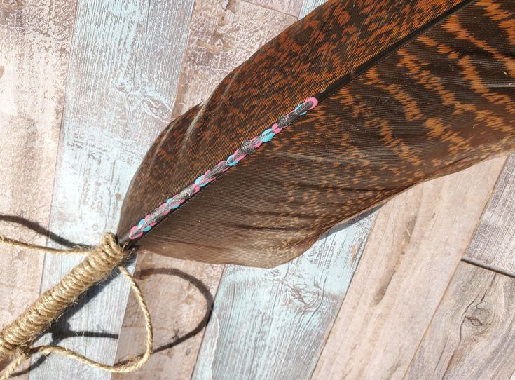 a brown feather with some beads on it sitting on top of a piece of wood