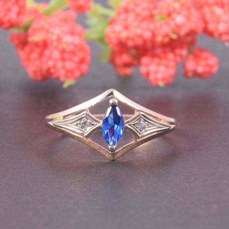 a gold ring with a blue stone in the center on a table next to flowers