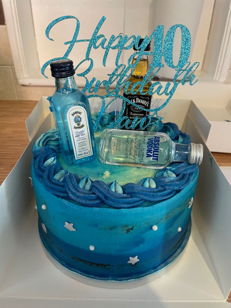 a birthday cake decorated with blue icing and liquor bottles in a box on top of a table