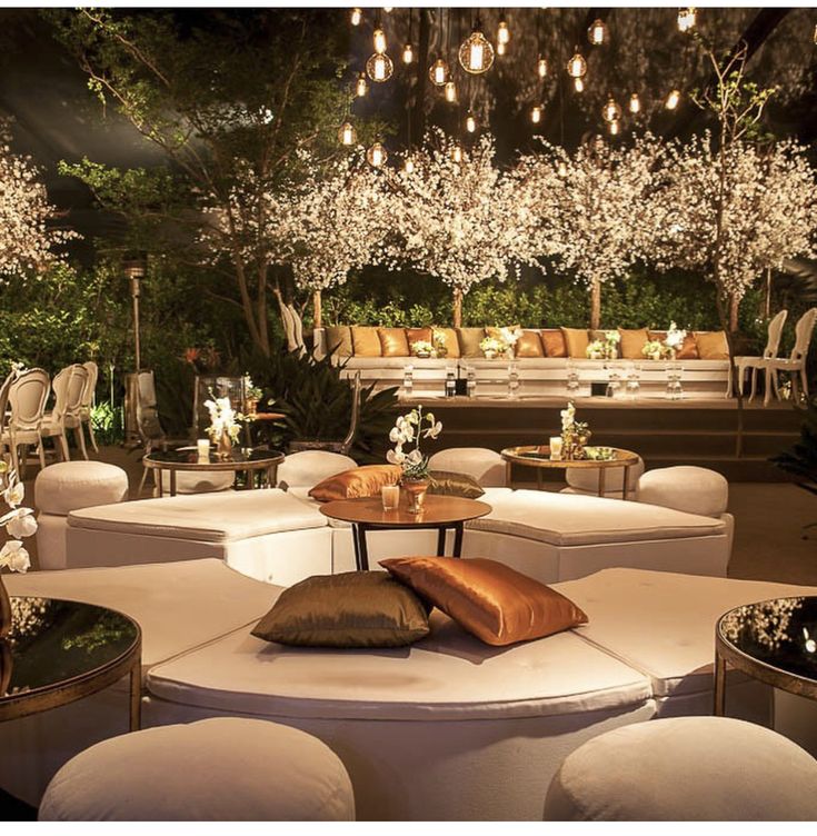 an outdoor seating area with white couches, tables and chandeliers hanging from the ceiling