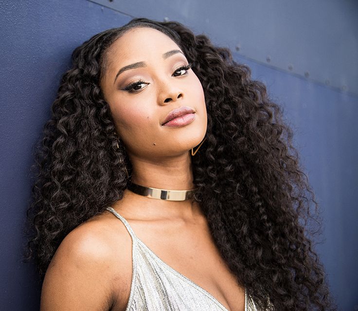 a woman with long curly hair wearing a choker and posing against a blue wall